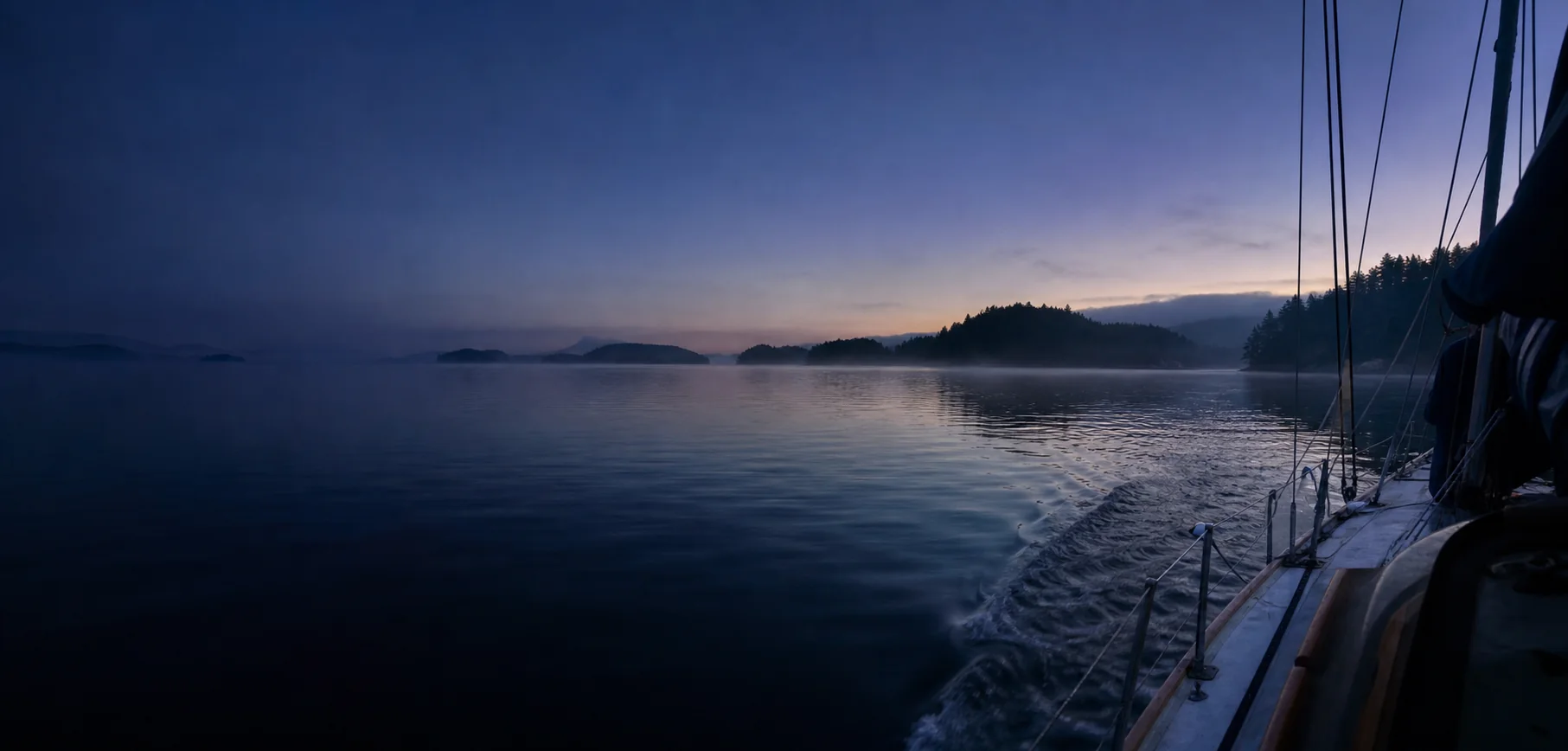 A sailboat moving through calm island waters at blue hour